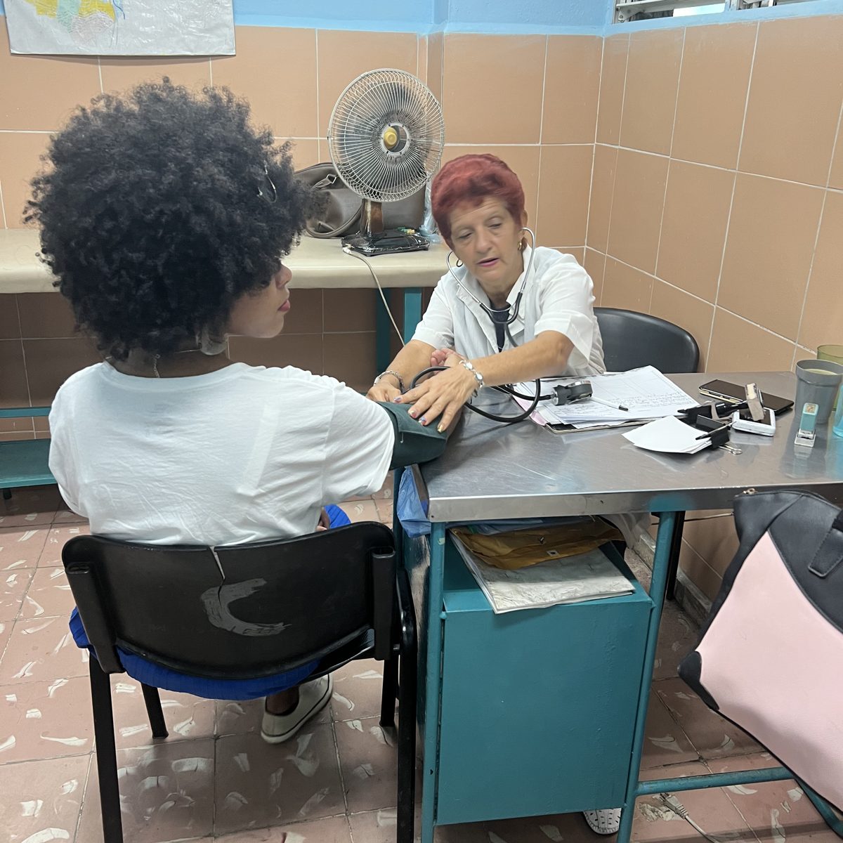 Uma profissional de saúde mede a pressão arterial de um paciente em uma mesa de clínica.