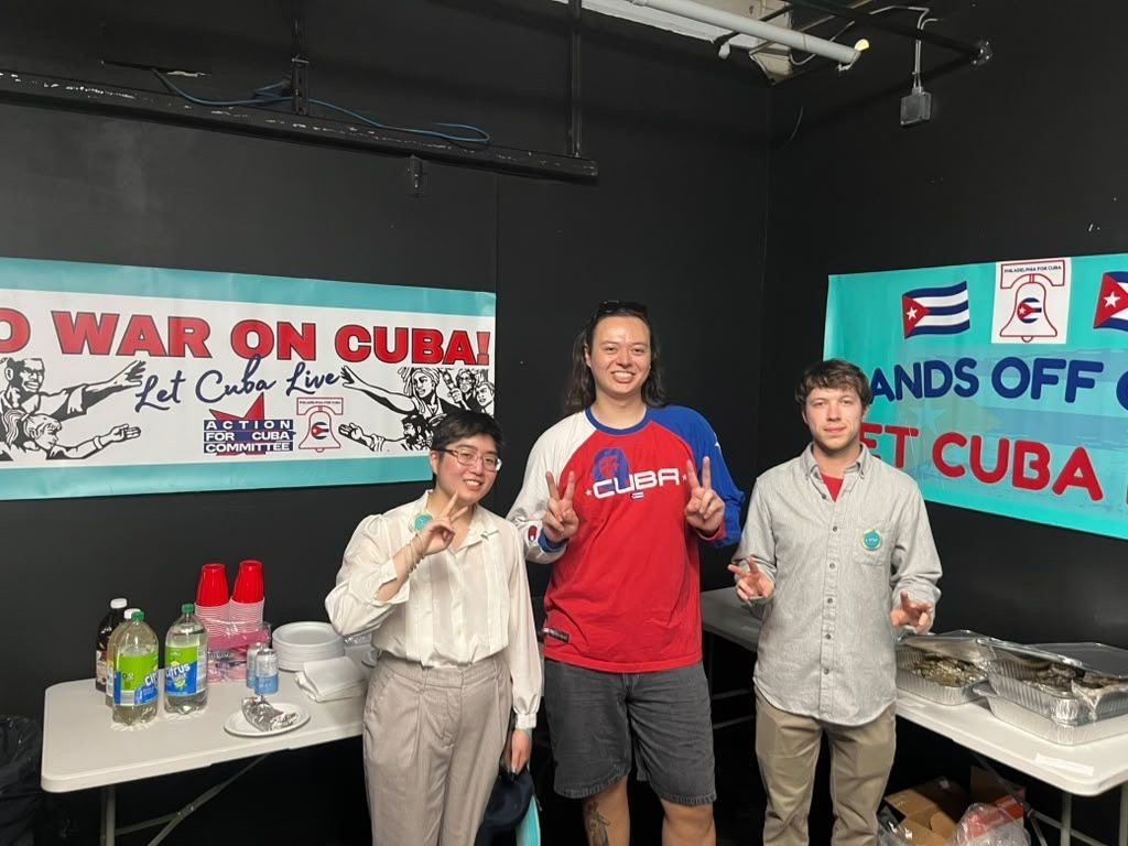 Three P4C organizers smile beside solidarity banners at an event.
