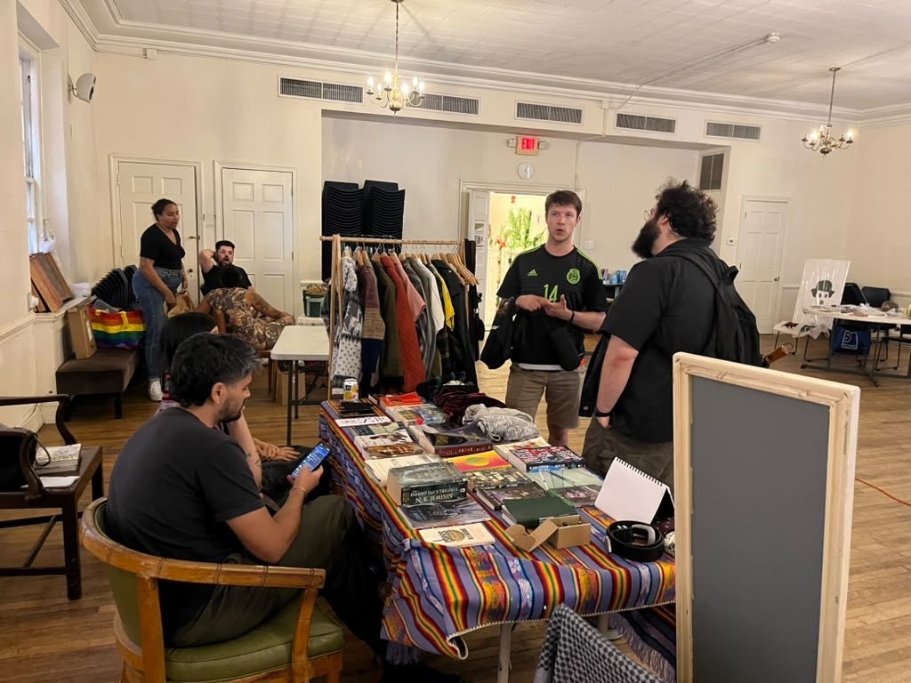 Volunteers talk with visitors beside a table of books and materials at a community event.