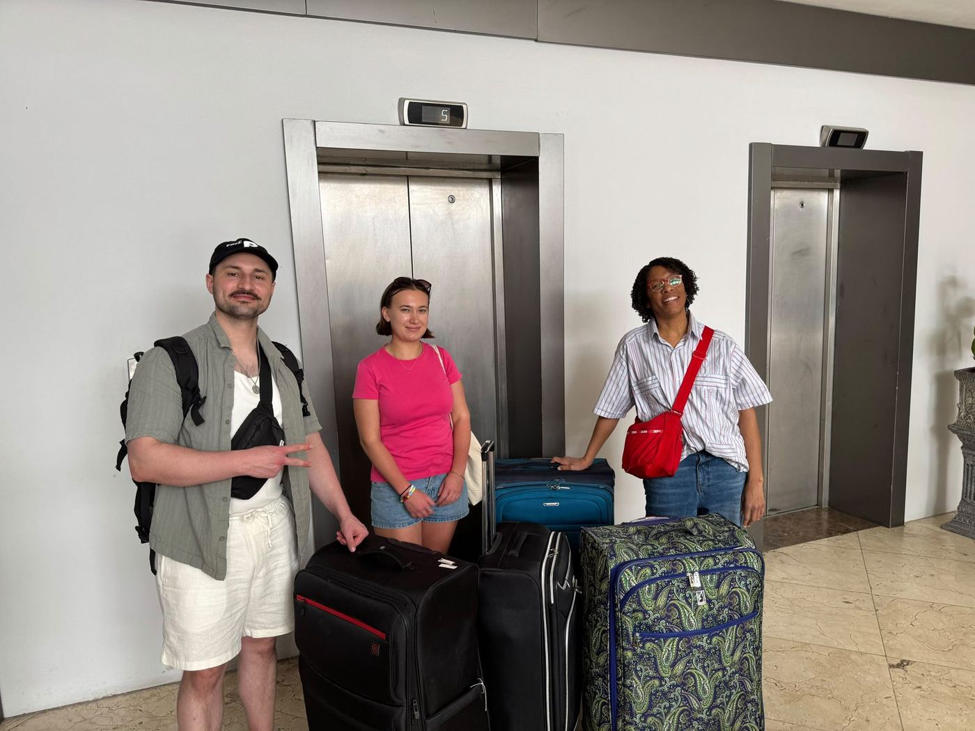 Three travelers stand with suitcases in a building lobby.