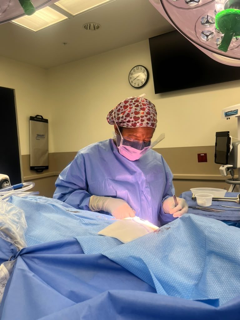 P4C founder Dr. Renee Quarterman, in surgical gown, mask and a heart-print scrub cap, operating under surgical lights.