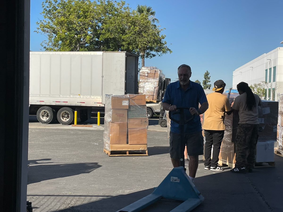 Volunteers move pallets of medical supplies toward a truck for shipping.